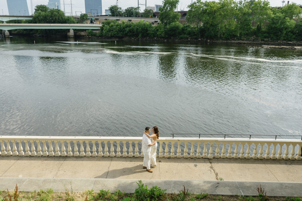 Elegant-couple-embracing-during-their-engagement-session-at-Fairmount-Water-Works-in-Philadelphia-with-the-Schuylkill-River-and-historic-architecture-in-the-background