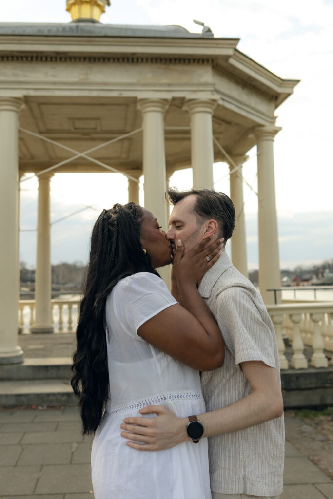 Elegant-couple-embracing-during-their-engagement-session-at-Fairmount-Water-Works-in-Philadelphia-with-the-Schuylkill-River-and-historic-architecture-in-the-background
